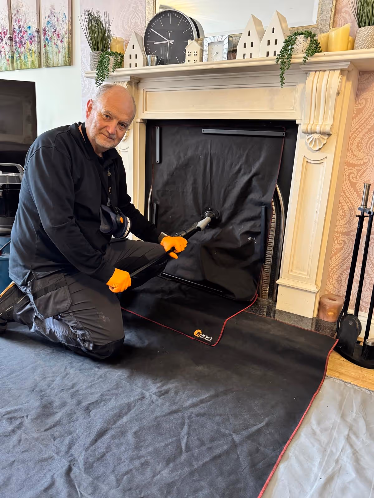Chimney sweep kneeling at a fireplace sealed with a black sheet, on a dust sheet