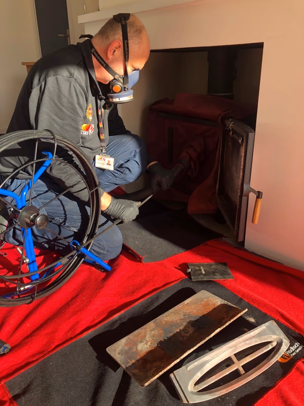 Chimney sweep in a dust mask sweeping a stove, with a power sweeping reel and red dust sheets